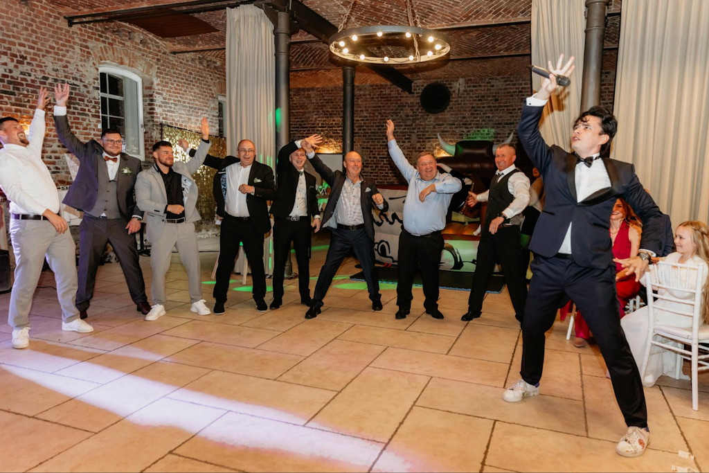 Hochzeitsmoderator und G&auml;ste tanzen mit erhobenen Armen auf der Tanzfl&auml;che einer Industrieloft-Location